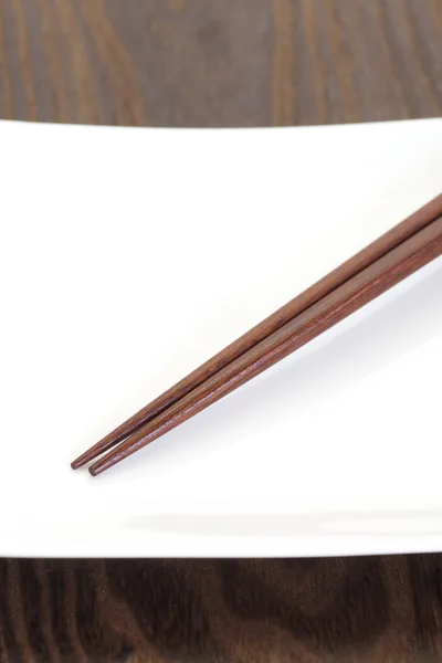 Vit platta och brunt trä chopstick — Stockfoto