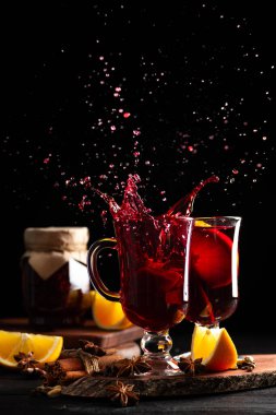 koyu ahşap arka planda baharatların arasına şarap döküldü, farklı yönlere saçılmış sıcak şarap damlaları.