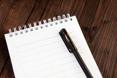 Beyaz bir spiralde bir not defteri ve siyah bir kalem eski bir arka planda.