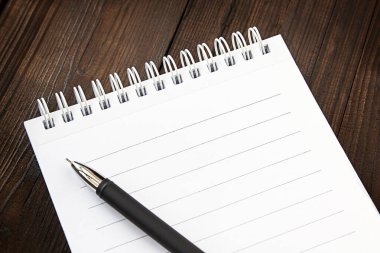 Beyaz bir spiralde bir not defteri ve siyah bir kalem eski bir arka planda.