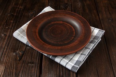 Beyaz kareli bir havlunun üzerinde boş bir kil plaka, koyu ahşap bir arka planda.