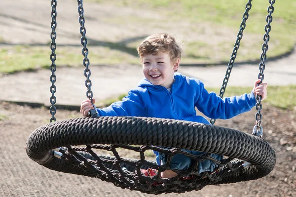 Šťastný chlapec houpající se na velký kulatý swing — Stock fotografie