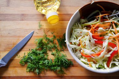 Seramik kasede sebze salatası pişirmek. Lahana, biber, havuç, dereotu ve zeytinyağı ile birlikte. Tahta arkaplan üzerine seçici odak 