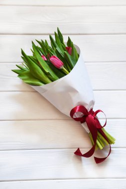 Beyaz ahşap arka planda kırmızı kurdeleli taze kokulu pembe lalelerden oluşan romantik bir buket.