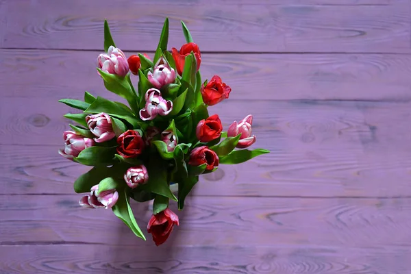 Bir bukette taze kırmızı ve pembe laleler, mor ahşap arka planda seçici bir odak