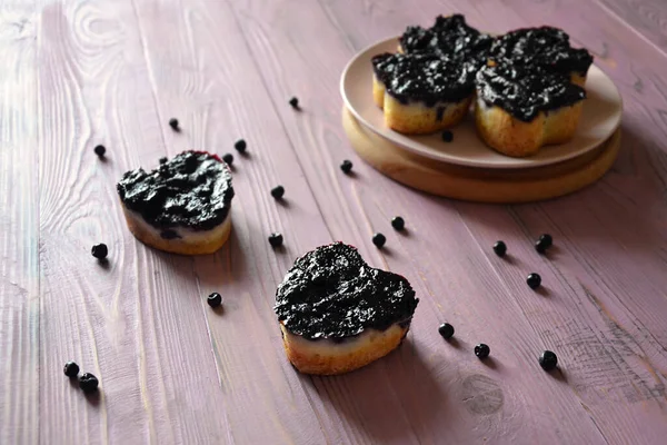 Mor ahşap masadaki yabanmersinli ev yapımı kalp şeklinde kekler, seçici bir odak noktası.