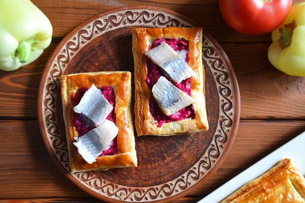 Yuvarlak kırmızı tabakta pancar salatası ve ringa balıklı iki ev yapımı puf böreği.