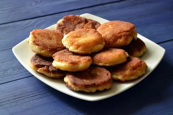 Mavi ahşap arka planda beyaz tabakta bol yağda kızartılmış süzme peynir krepleri, seçici odak