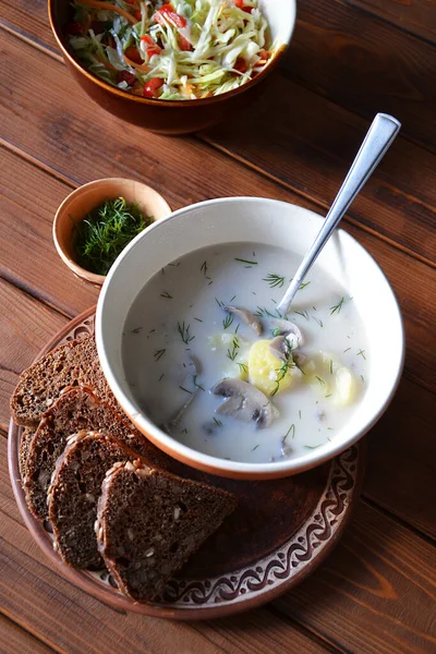 Hot home cooked mushroom soup with cheese, potatoes and dill in the clay bowl with rye bread on the wooden table top view