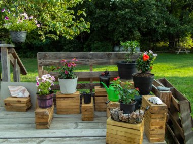 Eski bir güvertede bulunan ahşap bir bitkinin çiçek dizaynına yakından bakmak huzur ve neşe hissi verir. Arka planda piknik masası ziyaretçileri karşılıyor..