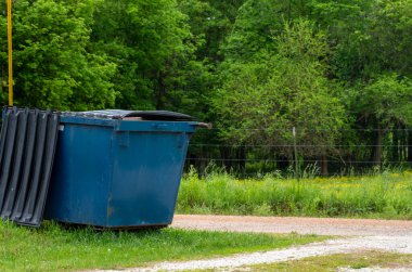 Büyük mavi bir çöp konteynırı, Missouri 'deki bu köy yolundaki kirliliği ortadan kaldırmak için mükemmel bir çöp kutusu. Bokeh etkisi.