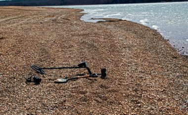 Alçak göl suları, bir metal dedektörü teknolojisiyle hazine avı için bol miktarda kıyı şeridi sağlar. Ekipmanlar bir mola sırasında gevşek çakılların üzerinde boş duruyor..