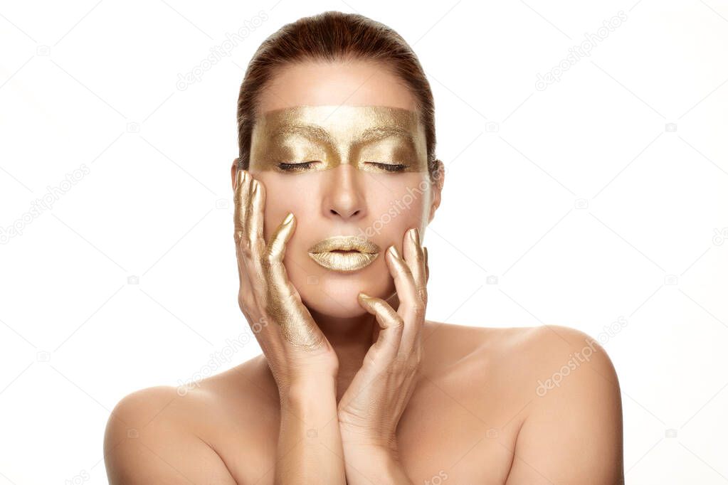 Gold based skincare concept. Beauty spa woman face with gold mask on eyes, lips and fingers holding her hands gracefully by the sides of face with closed eyes in a sensual gesture. Isolated on white