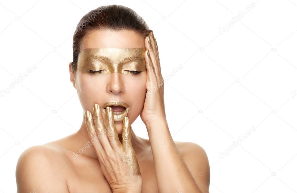 Gold based skincare concept. Beauty spa woman with gold mask on eyes, lips and fingers holding her hands gracefully by the sides of face with closed eyes in a sensual gesture. Isolated on white