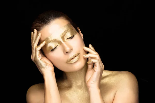 Gold based skincare concept. Beauty spa woman face with gold mask on eyes, neck and lips holding her hands gracefully by the sides of face with closed eyes in a sensual gesture. Isolated on black