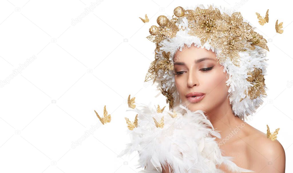 Beautiful model girl with golden Christmas hairstyle surrounded by golden butterflies, blowing magic dust on dainty white feathers. High fashion portrait of a fairy concept for xmas isolated on white