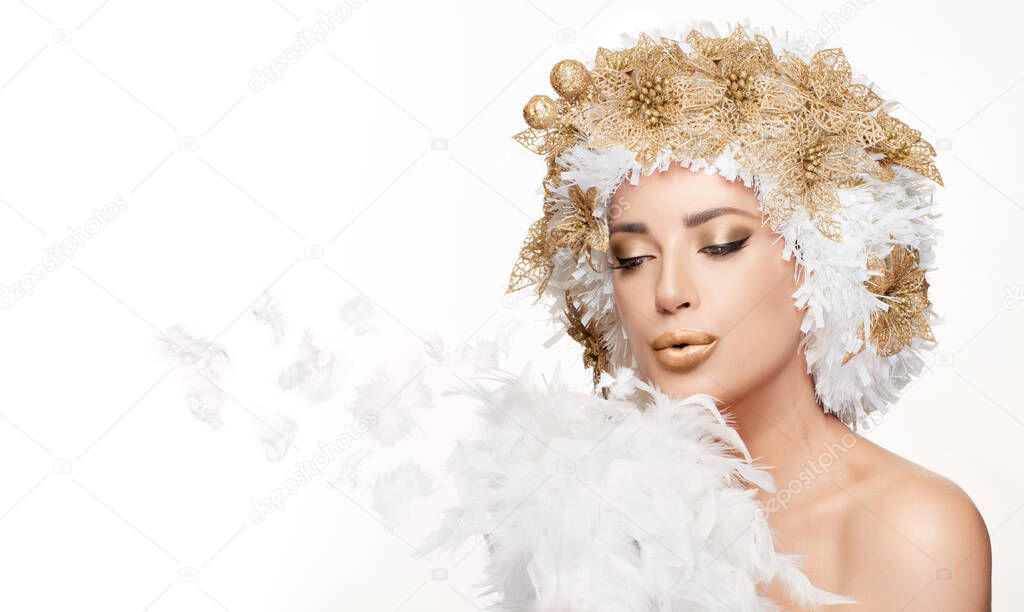 Beautiful winter fashion girl with a creative white and gold Christmas hairstyle and matching golden makeup blowing white feathers over copy space. Beauty portrait isolated on white