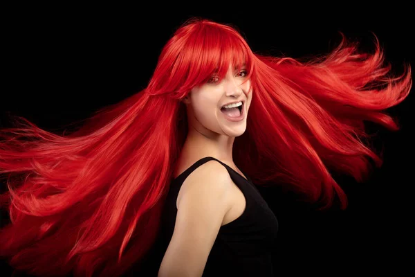 Beautiful young woman with long shiny red hair laughing while doing a twist to make her hair fly around face. Beauty face woman with healthy straight red hair in close up portrait isolated on black