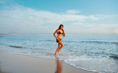 Kumsalda koşan ve egzersiz yapan bir kadın.