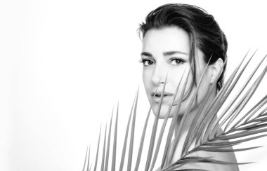 Omzunda tropikal bir yaprak tutan, kusursuz, taze derisi olan güzel bir kadın. Spa, sağlık ve cilt bakımı konsepti. Beyaz üzerine tek renkli resim ve kopyalama alanı