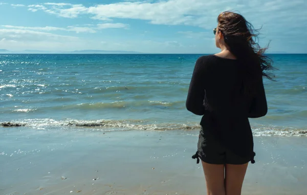 海辺の若い女性の後部ビュー彼女の髪を吹いて暖かい風を楽しんで — ストック写真