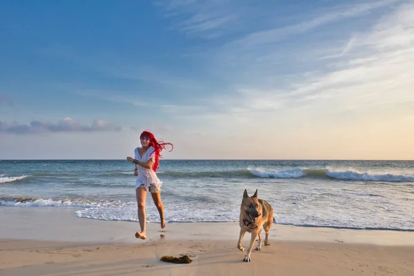 快乐的红头发女人 穿着休闲的夏装 带着她的狗在海滩上奔跑 — 图库照片