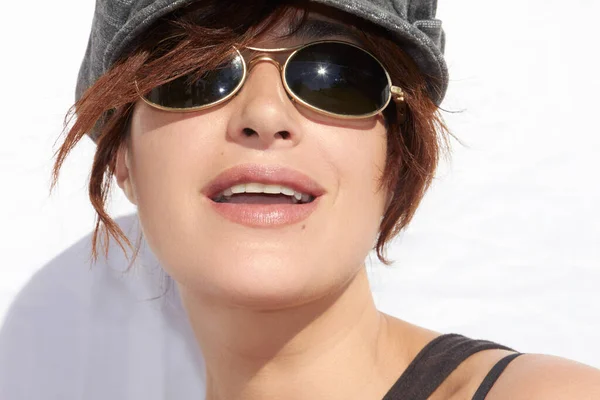 一个戴着时髦太阳镜 带着太阳镜 在夏日阳光下在白墙映衬下戴着顶灰色帽子 头戴阴影的漂亮女人的脸庞 — 图库照片