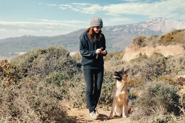 若い女性は丘や山で一緒に田舎の屋外で訓練中に彼女の犬に御馳走を提供します — ストック写真