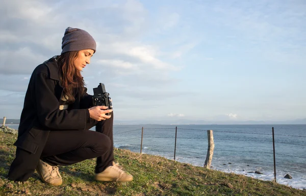 Jeune femme assise au bord de la mer tenant une caméra vintage — Photo