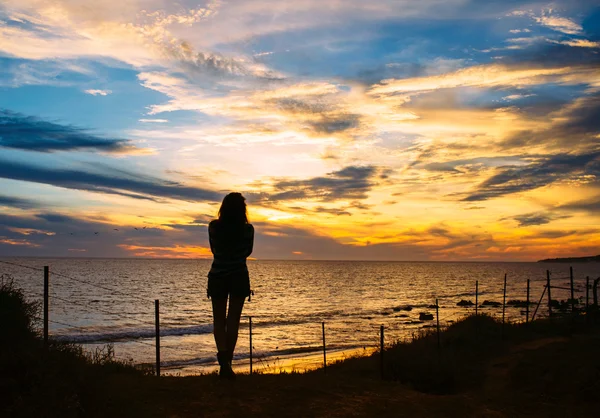 Silhouette de la femme se tient à la plage au coucher du soleil — Photo