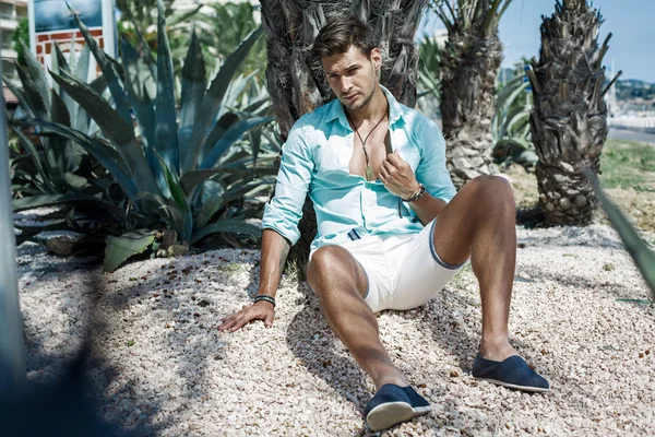 Handsome male model sitting under the palm tree — Stock Photo, Image