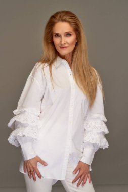 Gri stüdyo arka planında beyaz tişört giyen uzun düz saçlı olgun bir kadın model.