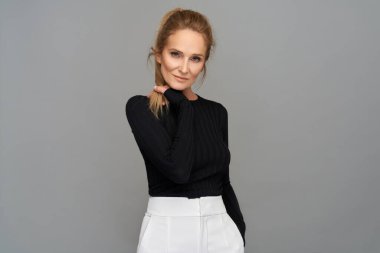 Gri arka planda yetişkin bir kadın model kameraya bakıyor.