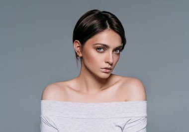 Kısa saçlı, gri arka planda izole genç, şehvetli esmer kadının stüdyo çekimi.