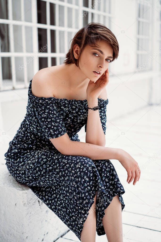 Young fashionable girl with short hair sitting outdoor in long stylish dress