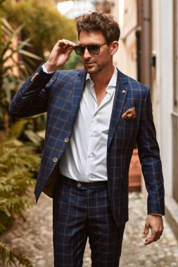 Sınıftaki yakışıklı adam güneş gözlükleriyle sokakta yürürken takım elbisesini kontrol etti. 