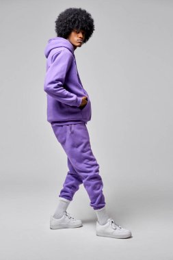 Genç siyah adamın hip-hop tarzı gri arka planda izole edilmiş mor eşofman takımı giyer.