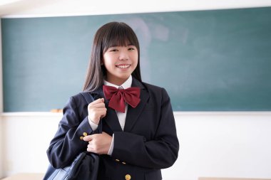 Sınıfta okul çantasını tutan bir Japon liseli kız.