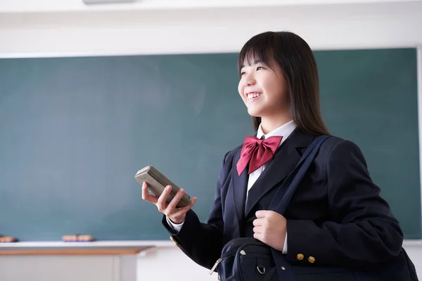 A Japanese junior high school girl smiles as she operates her phone in the classroom