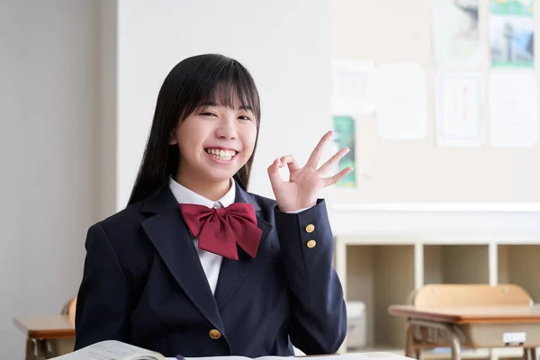 A Japanese junior high school girl strikes an OK pose in the classroom.