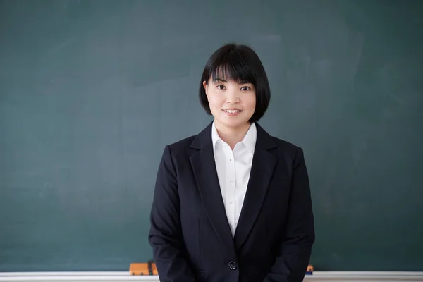 A Japanese woman teacher stands in front of the blackboard in her classroom