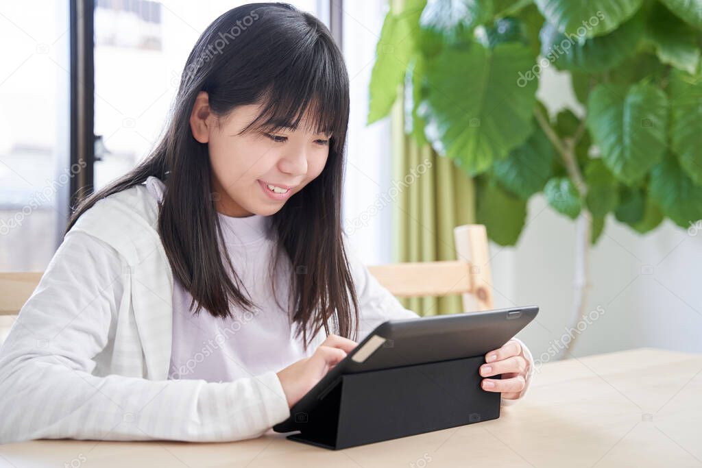 Junior high school Japanese girl watching a tablet in her living room
