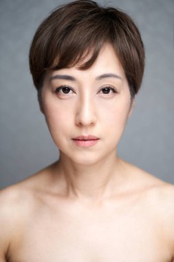 Orta yaşlı bir Japon kadın doğrudan kameraya bakıyor.
