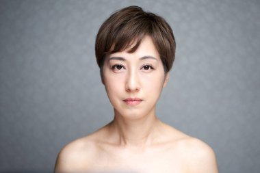 Orta yaşlı bir Japon kadın doğrudan kameraya bakıyor.