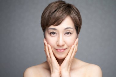 Orta yaşlı bir Japon kadın iki eliyle yanaklarının nemini kontrol ediyor.