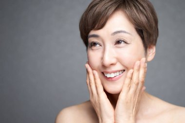 Gülümseyerek ellerini yanaklarına koyan orta yaşlı bir Japon kadın.