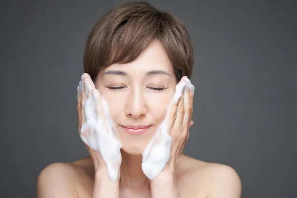 Orta yaşlı Japon kadın köpükle yüzünü yıkıyor.