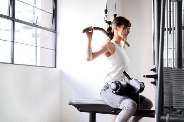 Asian woman doing back lat pull-down in training gym clipart