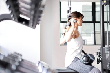 Asian woman doing back lat pull-down in training gym