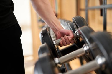 Asyalı bir adamın elleri raftan dambıl alıyor.